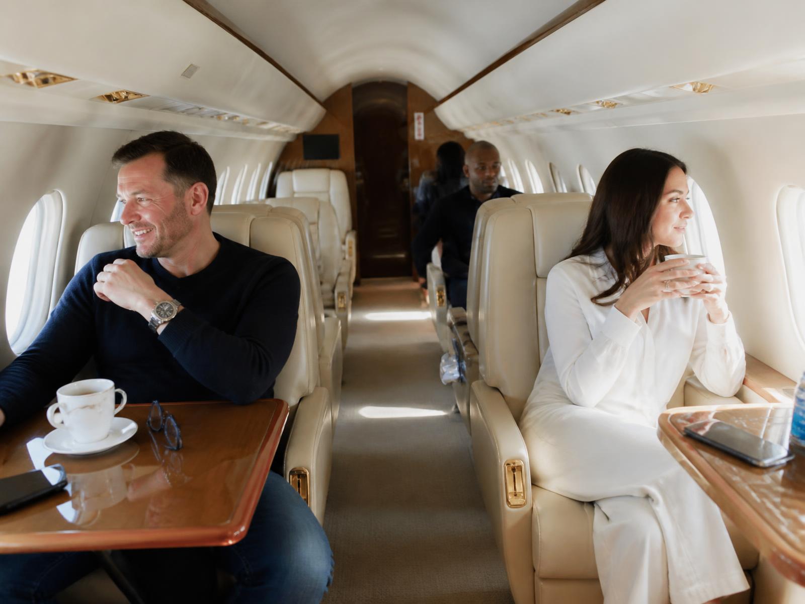 Cabin of a private jet with cream leather seats above the clouds