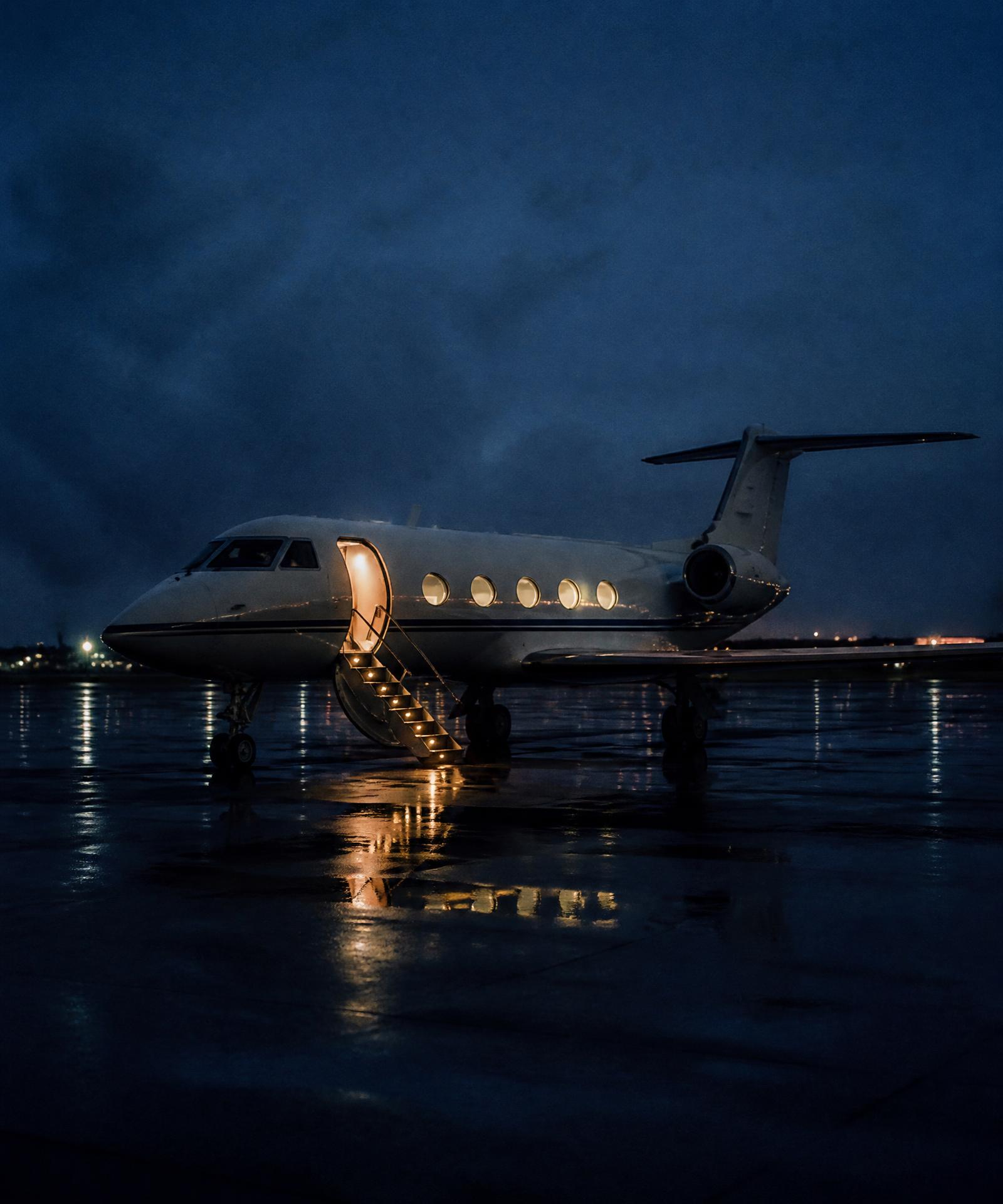 Private jet with the airstair lit on a rain-slicked apron at night